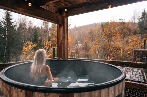 Vrouw met lang blond haar ontspant in een buitenbad bij Nutchel Lodges, Ardennen, België, met herfstlandschap.