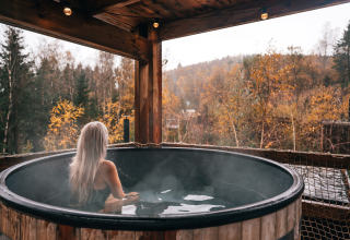 Frau mit langem, blondem Haar entspannt im heißen Outdoor-Bad bei Nutchel-Lodges in den Ardennen, Belgien.