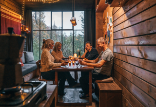 Quatre personnes partagent un repas chaleureux dans un chalet en bois des Nutchel - Lodges dans les Ardennes, Belgique.