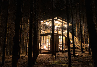 Verlichte Nutchel-lodge in het bos van de Ardennen, België, 's nachts. Ideaal voor bijzonder glampen.