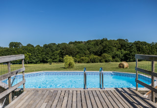 Swimming pool with wooden deck and handrails overlooking fields, Domaine Bonneblond Glamping Lodges Auvergne-Rhône-Alpes.