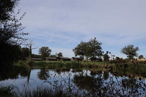 Glamping lodges at Domaine Bonneblond in Auvergne-Rhône-Alpes, set by a tranquil lake with trees and reflections.