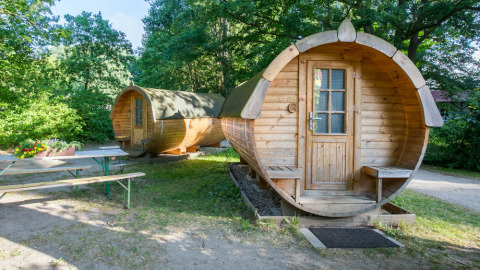 Twee houten pods in tonvorm als glampingaccommodatie bij Uhlenköper-Camp Uelzen, omringd door groen bos.