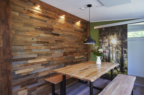 Modernes Glamping-Esszimmer mit Holzdekorwand, rustikalem Holztisch, Bank, Lampe und Blumenvase.