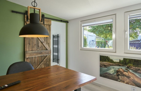 Hébergement glamping moderne avec table en bois, suspension, porte grange et vue sur le camping.