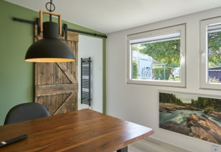 Moderne glamping-indkvartering med træbord, hængende lampe, lade dør og udsigt til campingplads.