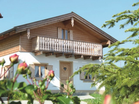 Charming lodge with wooden balcony at VITAL Camping Bayerbach, surrounded by greenery and flowers in Bavaria.
