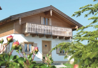 Lodge en bois avec balcon au VITAL Camping Bayerbach, entourée de fleurs et verdure en Bavière.