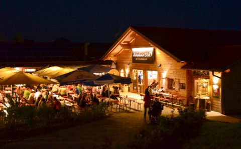 Avondeten buiten bij VITAL Camping Bayerbach - Lodges in Beieren, gezelligheid onder parasols met verlichting.