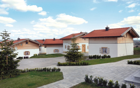 Vital Camping Bayerbach - Lodges in Bavaria with red rooftops, green lawns, and clear sky filled with clouds.