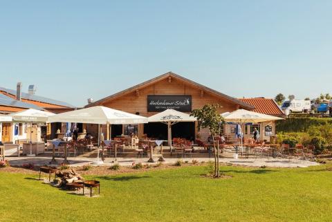 Outdoor dining terrace with umbrellas at VITAL Camping Bayerbach - Lodges in Bavaria, surrounded by greenery.