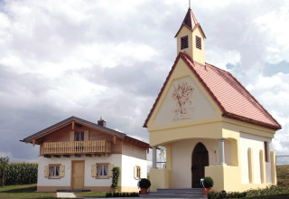 Due edifici affascinanti, una lodge e una piccola cappella, a VITAL Camping Bayerbach in Baviera sotto un cielo nuvoloso.