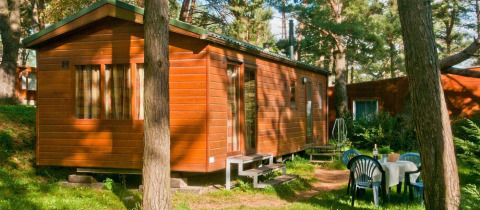 Houten stacaravan in het bos met buitentafel en stoelen bij Vakantiepark Havelberge - Stacaravan Orlando glamping.