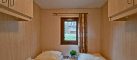 To enkeltsenge i et lyst træbeklædt værelse med vindue og udsigt til natur i Vakantiepark Havelberge.