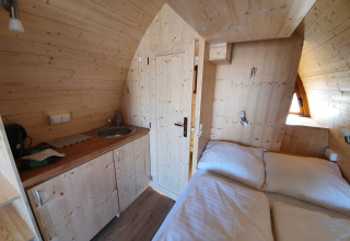 Interior view of a cozy wooden glamping pod with kitchenette and bed at Campingplatz Auf dem Simpel.