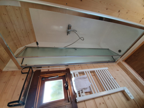 Modernes Badezimmer mit Badewanne, Glasduschwand, Fenster und Handtuchheizkörper in einer Holzhütte.