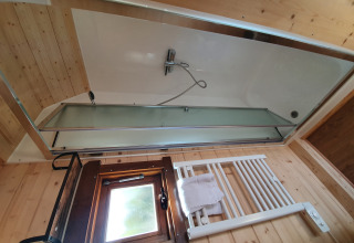 Modern bathroom with bathtub, glass shower screen, towel radiator and window in a wooden glamping pod.