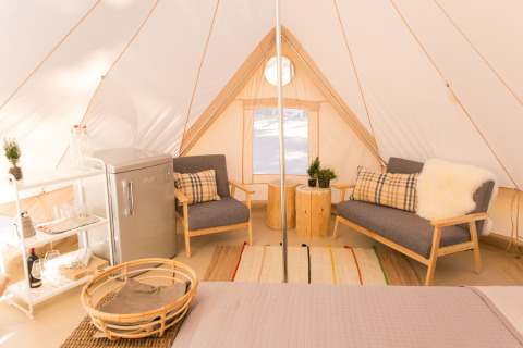 Indvendig udsigt over en luksuriøs glamping-telt med komfortable møbler, små planter og mini-køleskab.