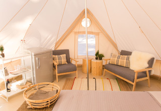 Indvendig udsigt over en luksuriøs glamping-telt med komfortable møbler, små planter og mini-køleskab.
