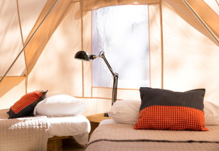 Intérieur d'une tente glamping au Camping Ca Savio - Nordisk Village Venise avec deux lits et lampe.