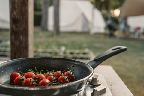 Padella con pomodori su fornello all’aperto, tende glamping sullo sfondo al Camping Ca Savio a Venezia.