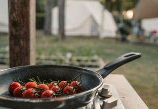Koekenpan met tomaten op een fornuis buiten, glamping tenten op de achtergrond bij Camping Ca Savio.