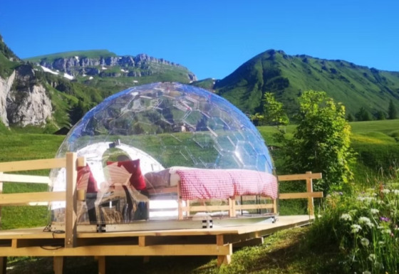 Glamping en un iglú de cristal Bubbelreis en Isenthal, Suiza, rodeado de montañas verdes y prados floridos.
