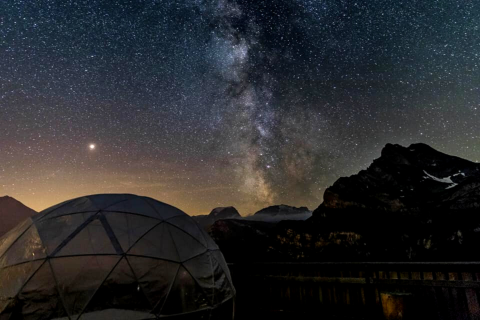 Alojamiento glamping: iglú de cristal en Isenthal con cielo estrellado y la Vía Láctea visible por la noche.