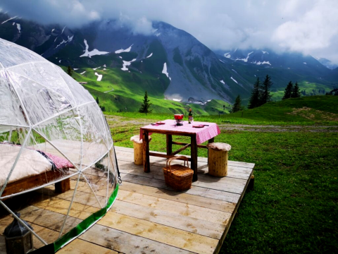 Glamping met glazen iglo, houten terras, picknicktafel en prachtig uitzicht op de Alpen en dal.