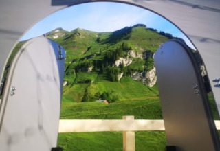 Zicht vanuit Bubbelreis - Glazen Iglo Isenthal door open deuren op groene bergen en blauwe lucht.