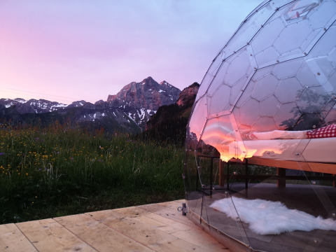 Glamping di lusso in igloo di vetro su terrazza in legno con vista montagna a Isenthal al tramonto.