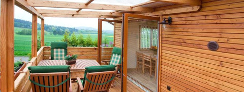 Terrazza in legno con sedie e tavolo al glamping Ferienanlage Erzeberg Blockhütten Hessen, vista campagna.