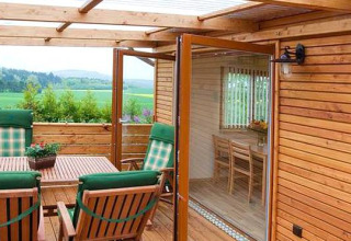 Houten terras met groene stoelen en tafel bij glamping Ferienanlage Erzeberg - Blockhütten Hessen, uitzicht veld.