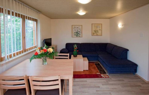 Sala de estancia en Ferienanlage Erzeberg - Blockhütten Hessen con sofá esquinero y mesa de comedor.