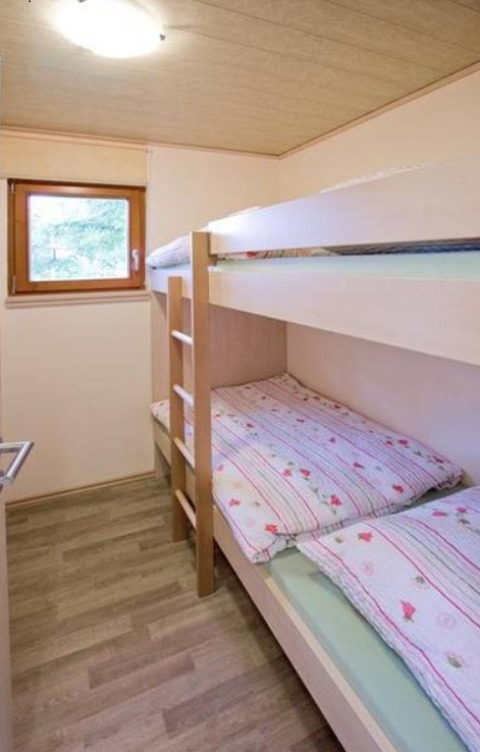 Et hyggeligt værelse i Ferienanlage Erzeberg - Blockhütten Hessen med køjeseng og vindue til naturen.