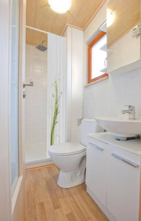 Baño compacto y luminoso con inodoro, ducha, lavabo y suelo imitación madera en cabaña glamping en Hessen.