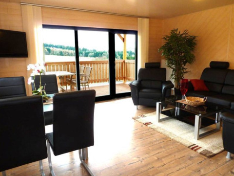 Modernes Wohnzimmer in einem Glamping-Blockhaus Hessen mit Ledersofas, Balkon und Naturblick.