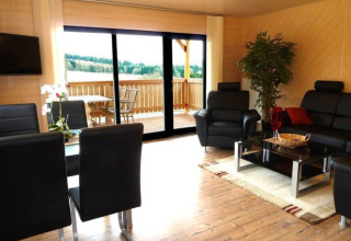 Soggiorno moderno in sistemazione glamping Blockhütten Hessen, con divani in pelle e vista balcone.