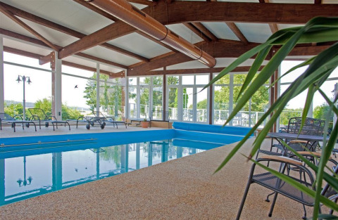 Piscina coperta con sedie a sdraio e ampie vetrate presso Ferienanlage Erzeberg - Blockhütten Hessen, immersa nel verde.