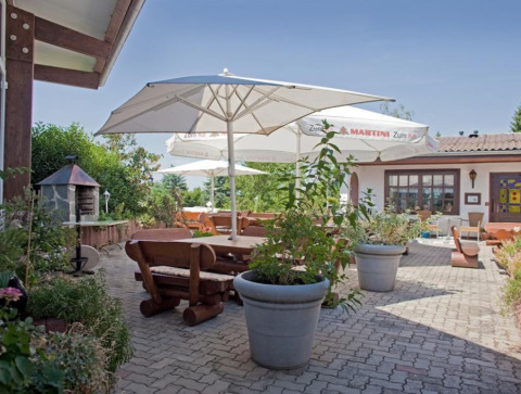 Terraza exterior en Ferienanlage Erzeberg - Blockhütten Hessen glamping con bancos de madera y sombrillas.