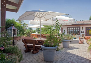 Outdoor terrace at Ferienanlage Erzeberg - Blockhütten Hessen glamping, featuring wooden benches and umbrellas.