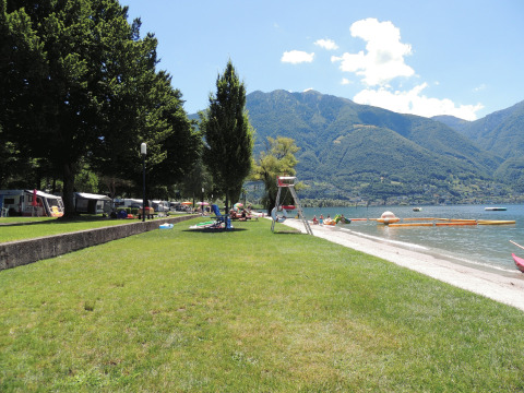 Vista del Campofelice Camping Village en Lago Maggiore con áreas verdes, playa y montañas al fondo.