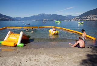 Børn leger ved søens bred, omgivet af oppustelige vandlegepladser på Campofelice Camping Village, Lago Maggiore.