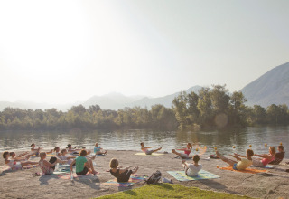 Gruppe mennesker laver udendørs træning på yogamåtter ved søen Campofelice Camping Village, Lago Maggiore.