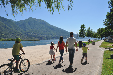 Gezin wandelt langs het meer in Campofelice Camping Village - Igloo Tube Lago Maggiore, met fietsen en steps.