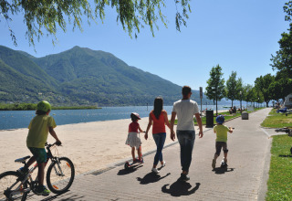 Famille marchant au bord du lac au Campofelice Camping Village - Igloo Tube Lago Maggiore par temps ensoleillé.