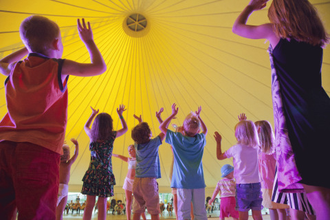 Kinderen dansen en spelen onder een grote gele tent bij Campofelice Camping Village - Igloo Tube Lago Maggiore.