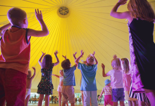 Kinder tanzen und spielen unter einem großen, gelben Zelt bei Campofelice Camping Village - Igloo Tube Lago Maggiore.