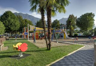 Playground at Campofelice Camping Village - Igloo Tube Lago Maggiore with mountain views and palm trees.