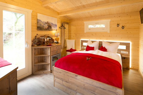 Gezellige glamping blokhut met houten interieur, tweepersoonsbed en rode accenten bij Campingpark Wiesenbeker Teich.